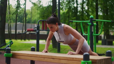 Female-athlete-doing-bench-push-ups-for-strength-workout-at-city-park-in-summer.-Sporty-woman-training-outdoor